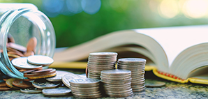 Glass jar spilling with coins next to an open text book