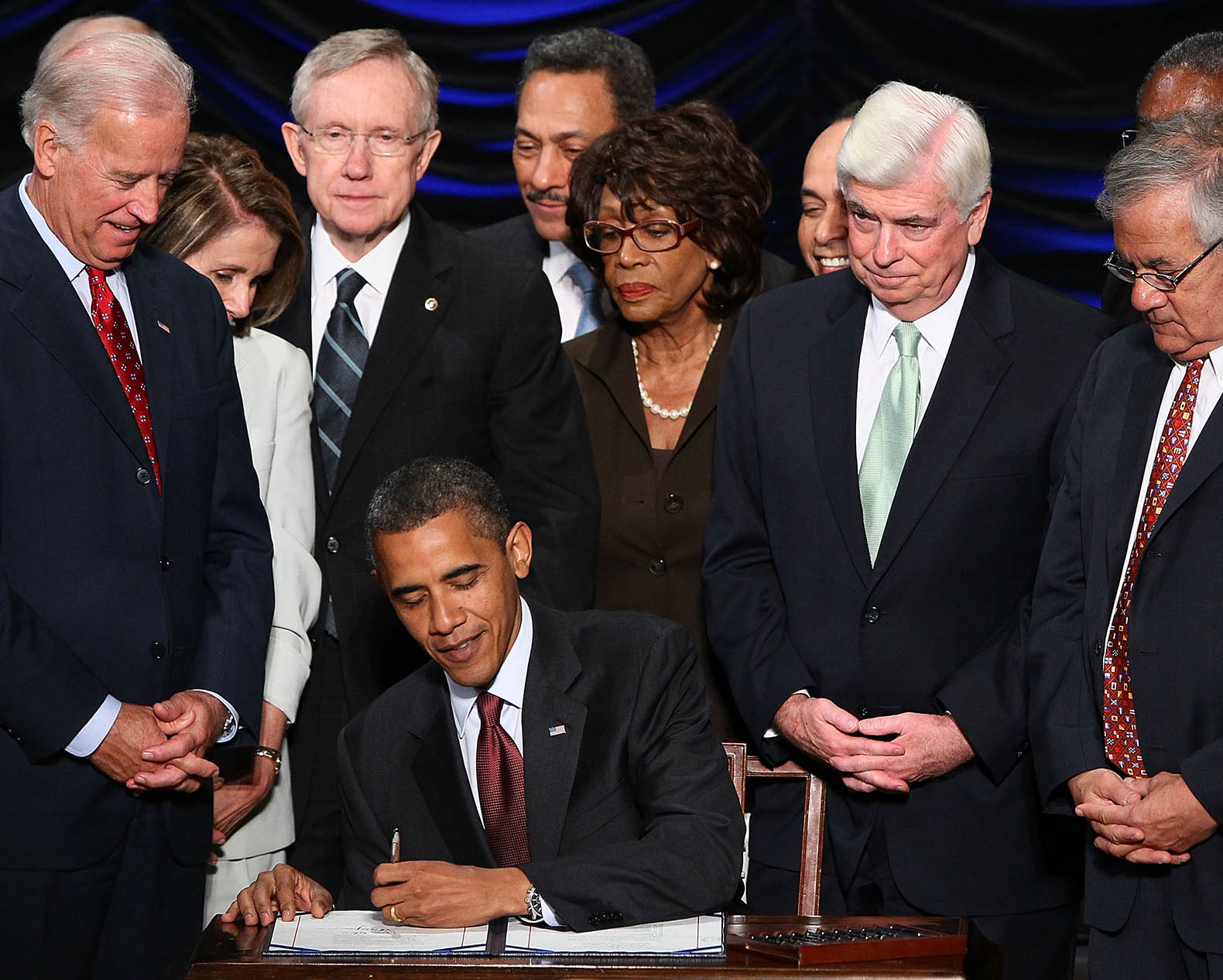 Barack Obama signing a bill with congress behind him.